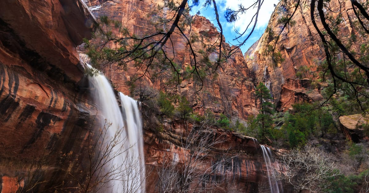 A seasonal waterfall spilling down striated red sandstone canyon walls in Zion National Park after rain.