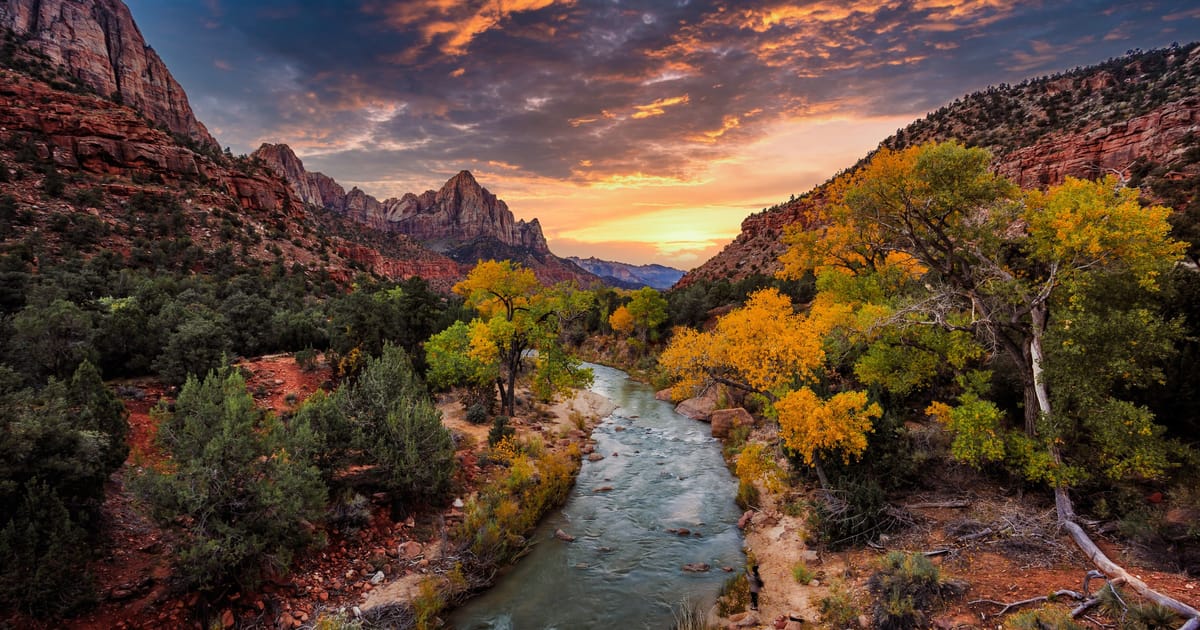 The Virgin River winding through Zion Canyon at sunset, the sandstone cliffs lit warm in low evening light.