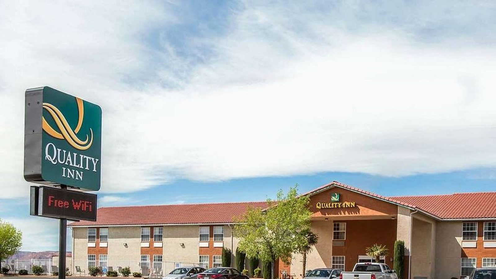 A Quality Inn hotel exterior is shown in a parking lot setting with a roadside sign advertising free WiFi.