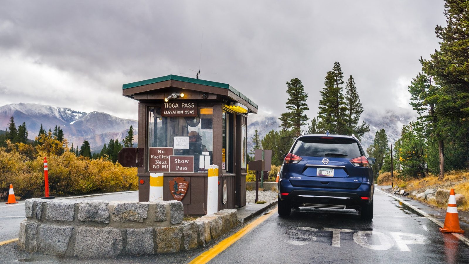 A Nissan Rogue SUV stops at the Tioga Pass entrance station of Yosemite National Park, elevation 9945 feet, on a moody overcast day with snow-dusted Sierra N…