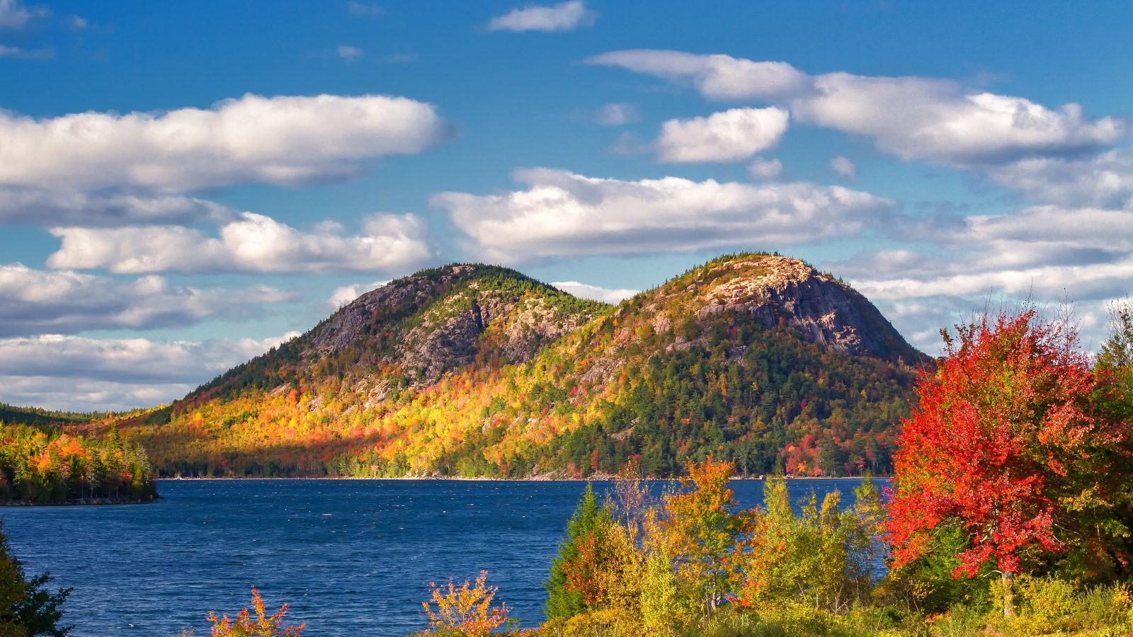 A stunning autumn view of the Bubbles twin summits rising above Jordan Pond in Acadia National Park, Maine, with vibrant fall foliage in red, orange, and gol…