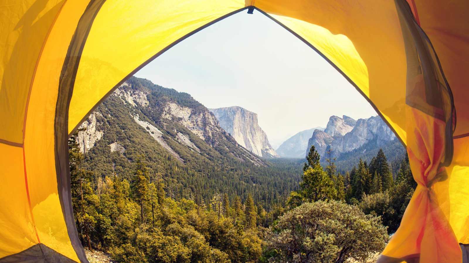 A breathtaking view of Yosemite Valley framed through the open doorway of a bright yellow camping tent, showcasing El Capitan and surrounding granite cliffs …