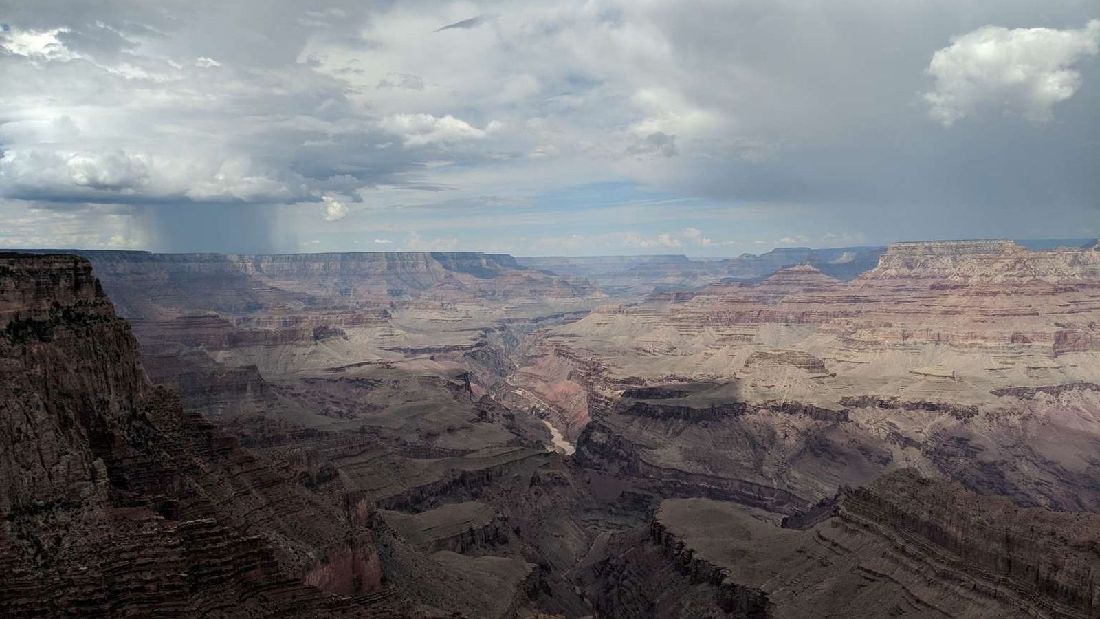 A vast panoramic view of the Grand Canyon from the South Rim, showing the layered red and tan sandstone formations descending to the Colorado River far below.