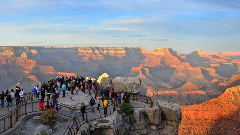 A panoramic view of the Grand Canyon's layered red and ochre sandstone formations stretching into a hazy blue distance, photographed from the South Rim near …