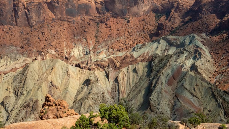 A dramatic aerial view into Upheaval Dome or a similar collapsed salt dome crater in canyon country, revealing striking multicolored badlands hills in green-…