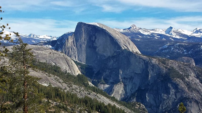 Half Dome's distinctive sheer granite face rises above a forested ridge in Yosemite National Park, with snow-dusted Sierra Nevada peaks stretching across the…