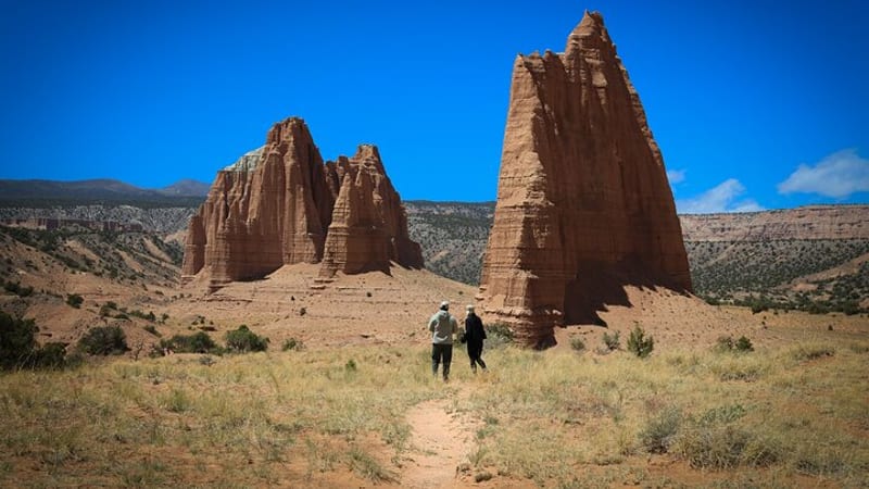 A historic pioneer farmstead with a rustic wooden barn and fenced pastures sits beneath towering red sandstone cliffs in Capitol Reef National Park, Utah.