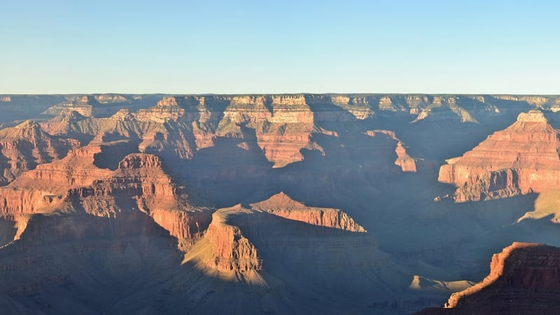 A winding, sediment-laden river flows through a deep canyon corridor flanked by towering red and tan sandstone cliffs, viewed from an elevated rocky vantage …